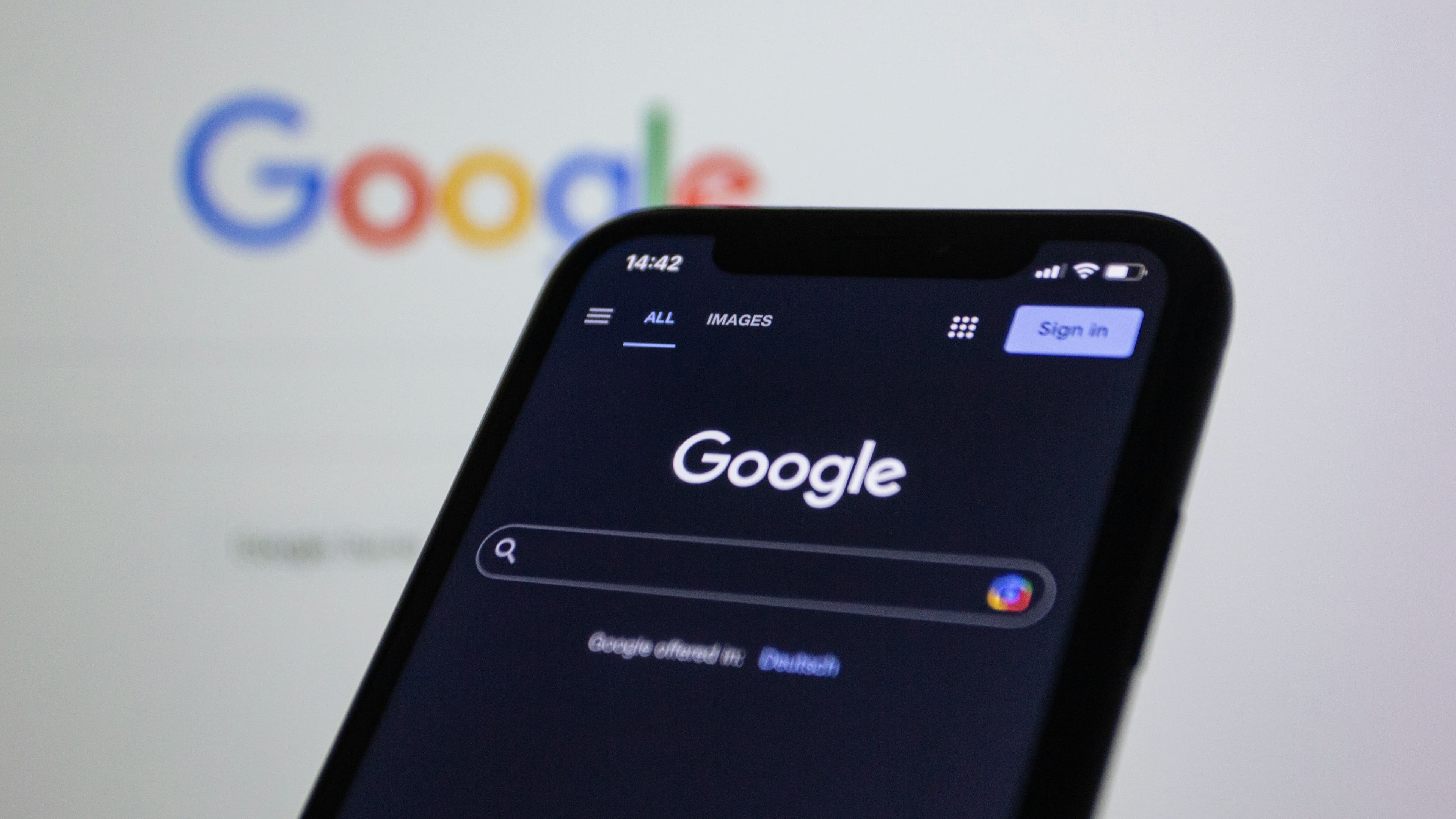 Handy vor einem Computerbildschirm. Sowohl das Handy als auch das Computer sind auf Google Search
